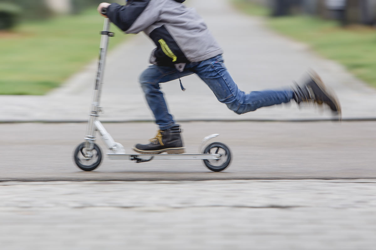 Halbkörper-Ansicht von einem Kind, das auf einem Tretroller fährt und mit einem Bein Schwung holt | Foto: Hanna Witte