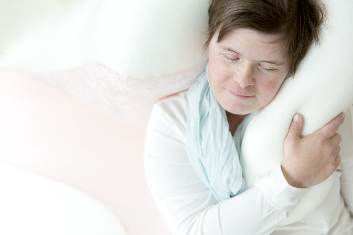 Foto einer Frau mit Down Syndrom, die mit geschlossenen Augen auf einem Kissen liegt | Foto: Hanna Witte