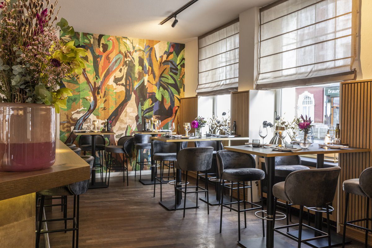 Innenansicht des Restaurant Stappen mit hohen Tischen und Barhockern vor einer bunt bemalten Wand | Foto: Hanna Witte