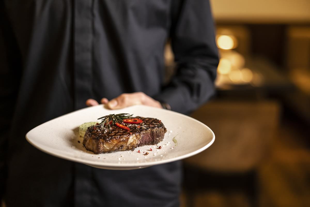 eine Servicekraft serviert ein gebratenes Steak mit Garnitur | Foto: Hanna Witte