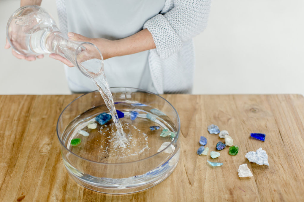eine Frau gießt Wasser in eine Glasschale mit Steinen und Kristallen | Foto: Hanna Witte