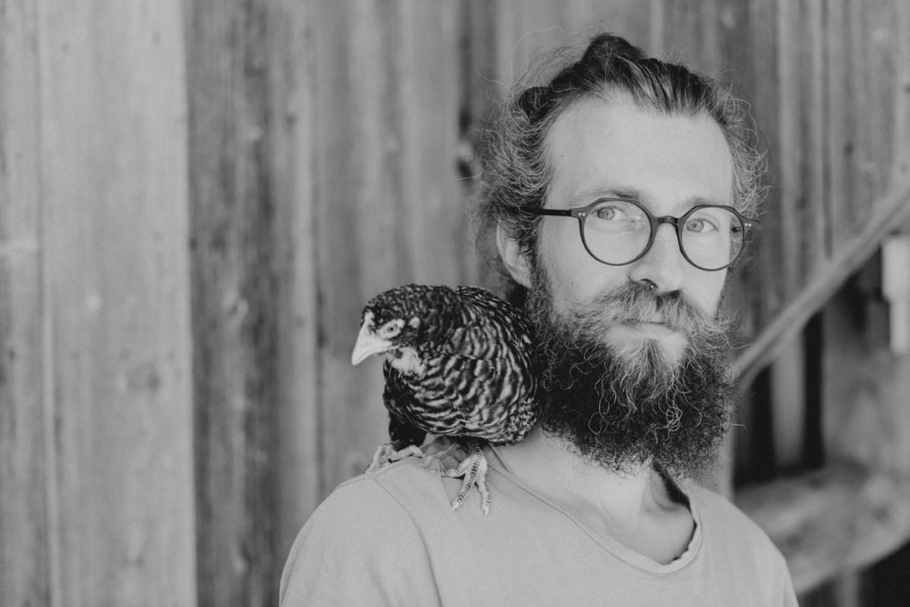 schwarz-weiss Portraitfoto von Roland Jensch mit einem Huhn auf der Schulter