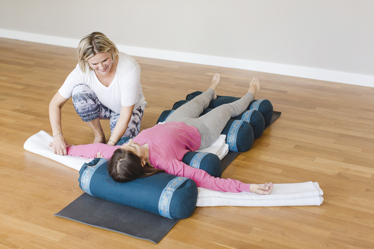 Foto einer Yogalehrerin bei einer Yogaübung mit einer Frau, die auf dem Boden liegt