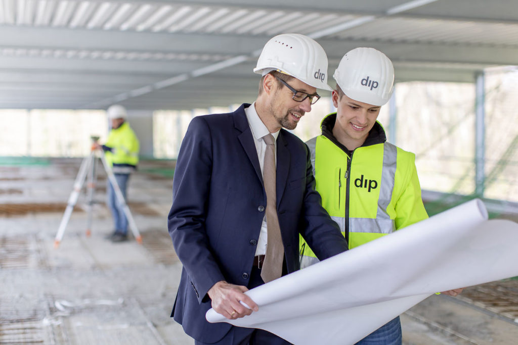 2 Mitarbeiter von dip studieren einen Bauplan auf einer Baustelle