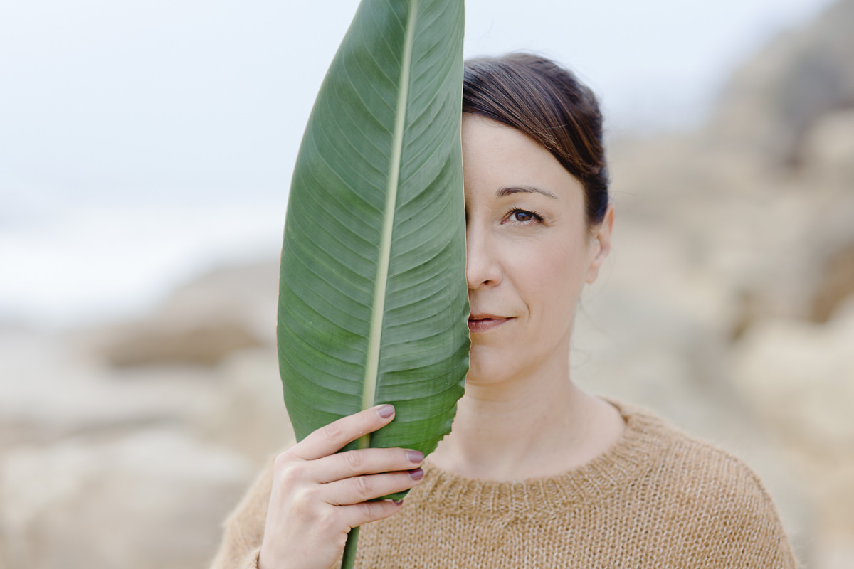 Portraitfoto von Yogalehrerin Christine Mack, die sich ein Blatt halb vor ihr Gesicht hält