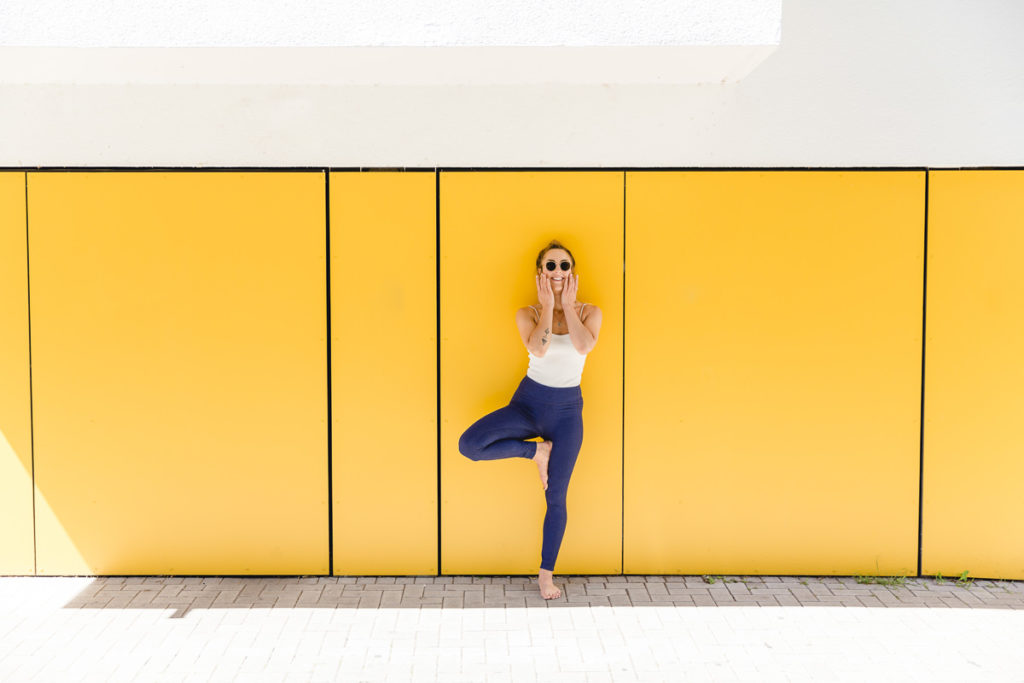 Yogalehrerin bei einem Outdoor Yoga Asana vor einer gelben Wand