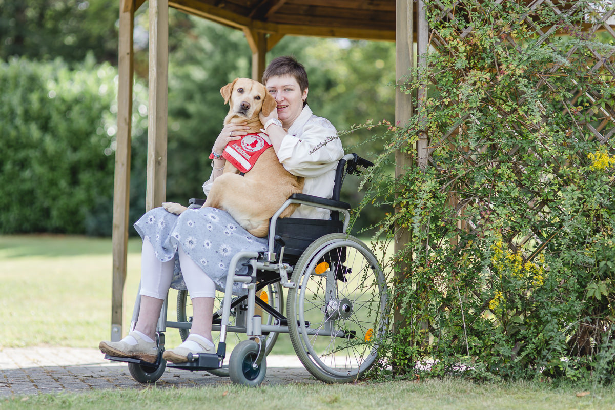 eine Patientin im Rollstuhl hat ihren Assistenzhund auf dem Schoß | Foto: Hanna Witte