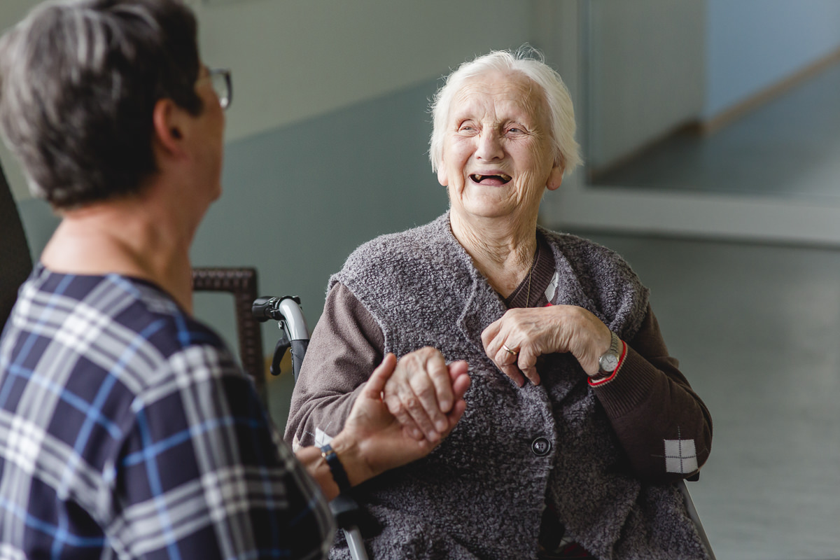 eine Betreuerin hält die Hand einer Seniorenheim Bewohnerin und lacht mit ihr | Foto: Hanna Witte