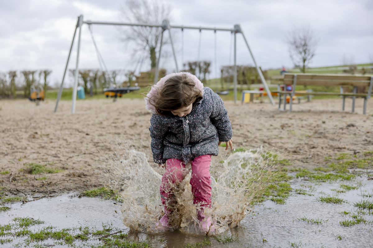 Familienhotel Fotografie Schlechtwetter-Urlaub: Ein Mädchen springt gut gelaunt in eine Regenpfütze | Foto: Hanna Witte