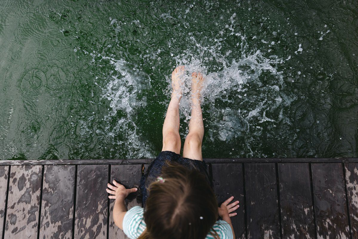 ein Kind sitzt auf einem Holzsteg und planscht mit den Füßen in einem Teich | Foto: Hanna Witte