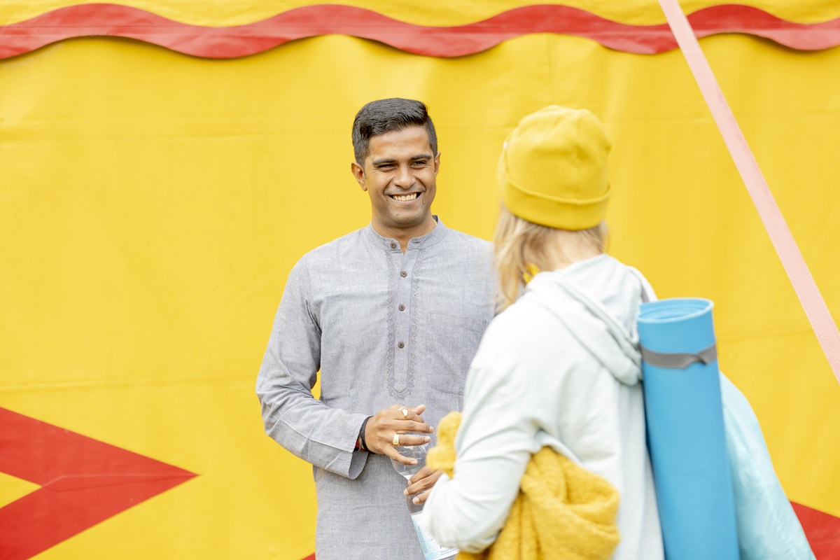 Ayurveda Heiler Dr. Vignesh Devraj spricht vor einem gelben Zelt mit einer Festival Besucherin | Foto: Hanna Witte