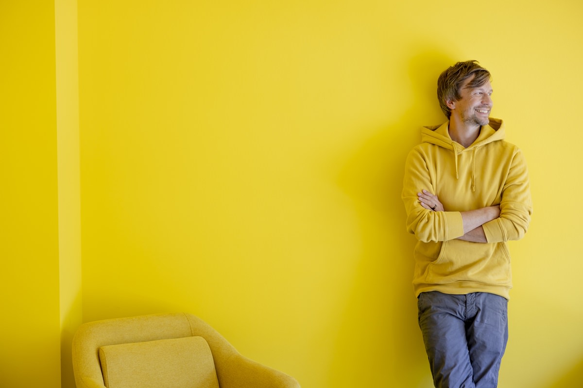 BabyOne Geschäftsführer Dr. Jan-Willem Weischer lehnt für ein Business Portrait entspannt an einer gelben Wand | Foto: Hanna Witte