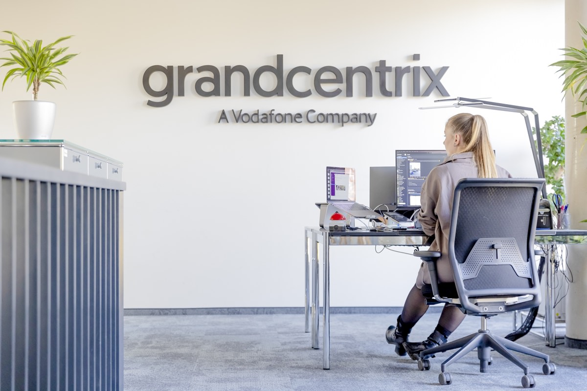 eine grandcentrix Mitarbeiterin arbeitet an ihrem Schreibtisch mit dem Firmenlogo im Hintergrund | Foto: Hanna Witte