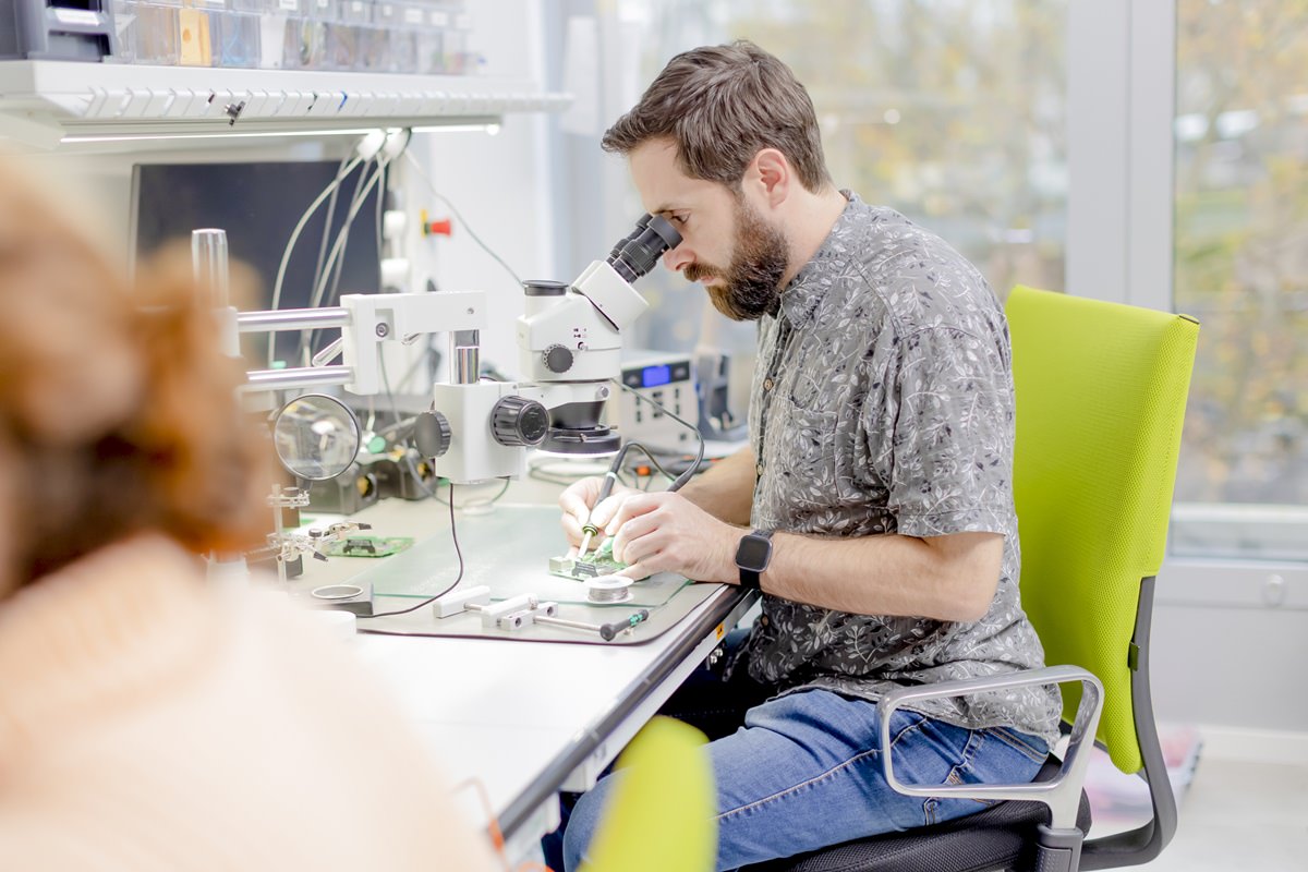 ein grandcentrix Mitarbeiter arbeitet mit einem Mikroskop an Hardware Produkten | Foto: Hanna Witte