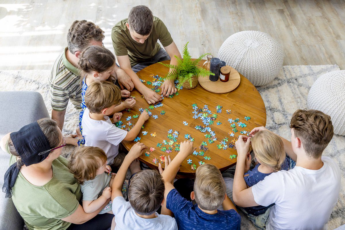 eine elfköpfige Familie macht gemeinsam ein Puzzle an einem runden Holztisch | Foto: Hanna Witte