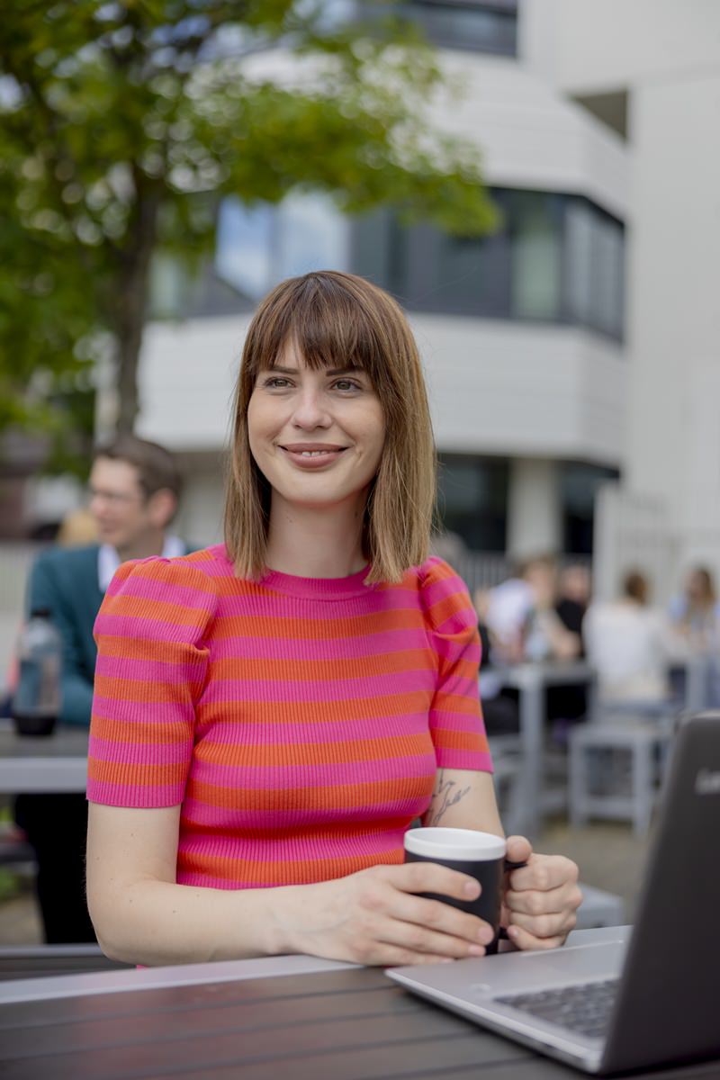 eine Studentin der Uni Siegen sitzt im Außenbereich der Uni und trinkt einen Kaffee | Foto: Hanna Witte