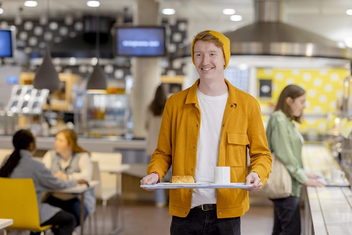 ein Student der Uni Siegen trägt in der Mensa ein Tablett mit Essen | Foto: Hanna Witte