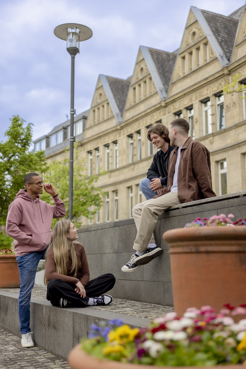 Studenten der Uni Siegen sitzen auf einer Mauer des Campus Geländes | Foto: Hanna Witte