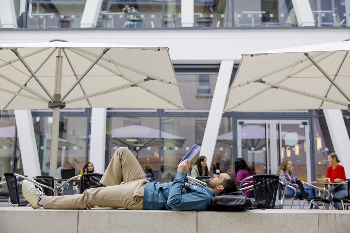 ein Student liest entspannt auf einer Mauer des Uni Siegen Campus | Foto: Hanna Witte