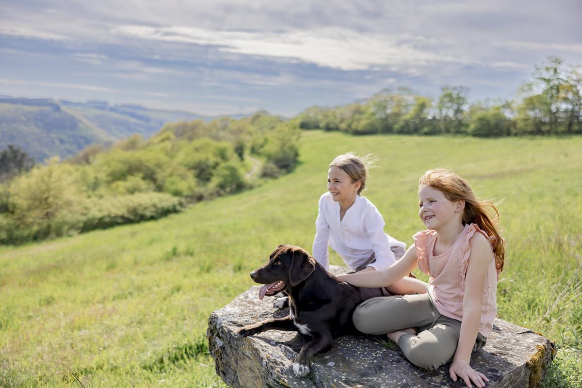 zwei Mädchen sitzen mit einem Hund auf einem großen Stein und schauen über die Wiese von Ferienhof Hardthöhe | Foto: Hanna Witte