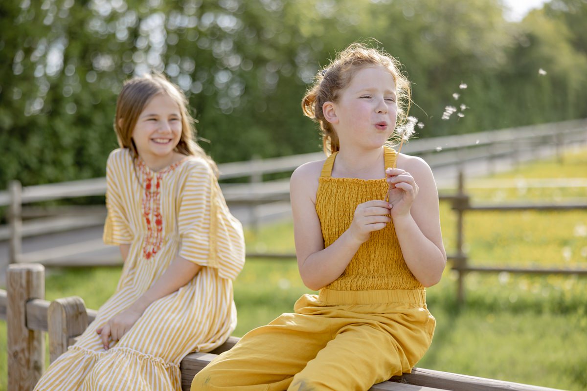 zwei Mädchen sitzen auf einem Holzzaun von Ferienhof Hardthöhe und pusten Pusteblumen | Foto: Hanna Witte