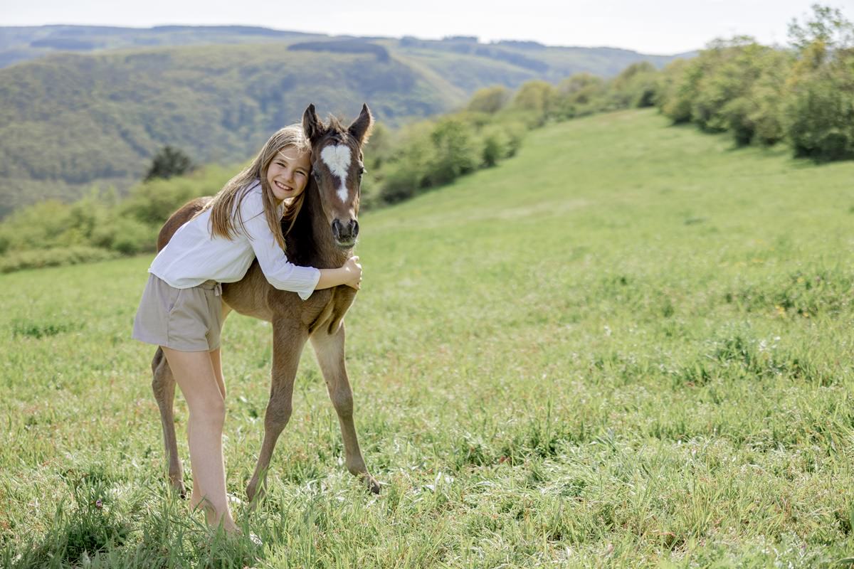 ein Mädchen umarmt ein Fohlen auf einer Wiese von Ferienhof Hardthöhe | Foto: Hanna Witte