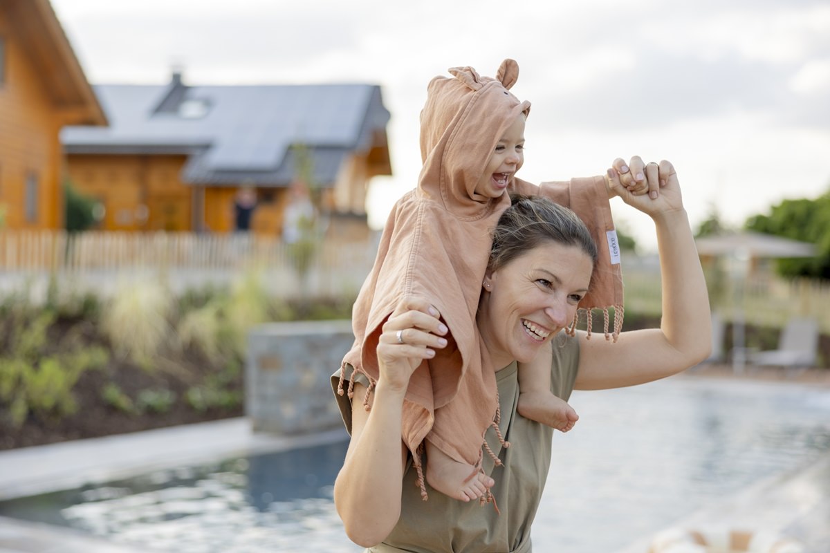 eine Mutter trägt ihr lachendes Kind auf den Schultern am Pool von Ferienhof Hardthöhe | Foto: Hanna Witte