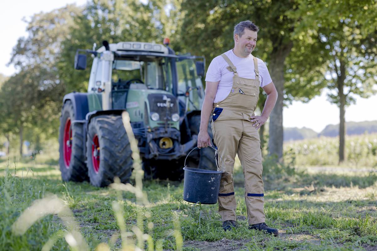 ein Landwirt steht mit einem Eimer in der Hand vor seinem Traktor | Foto: Hanna Witte