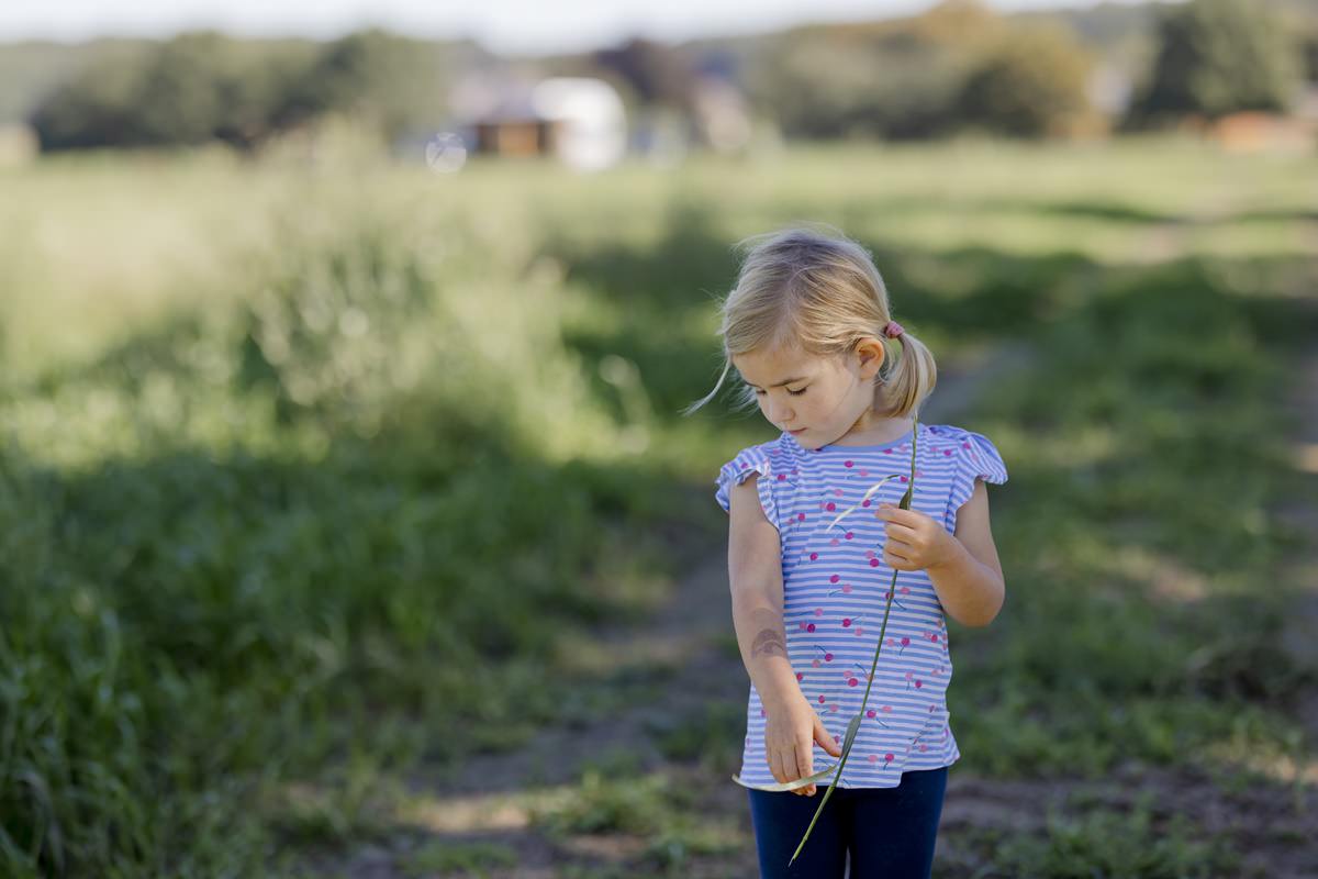 das Kind einer Landwirtsfamilie läuft mit einem Grashalm in der Hand über eine Wiese | Foto: Hanna Witte