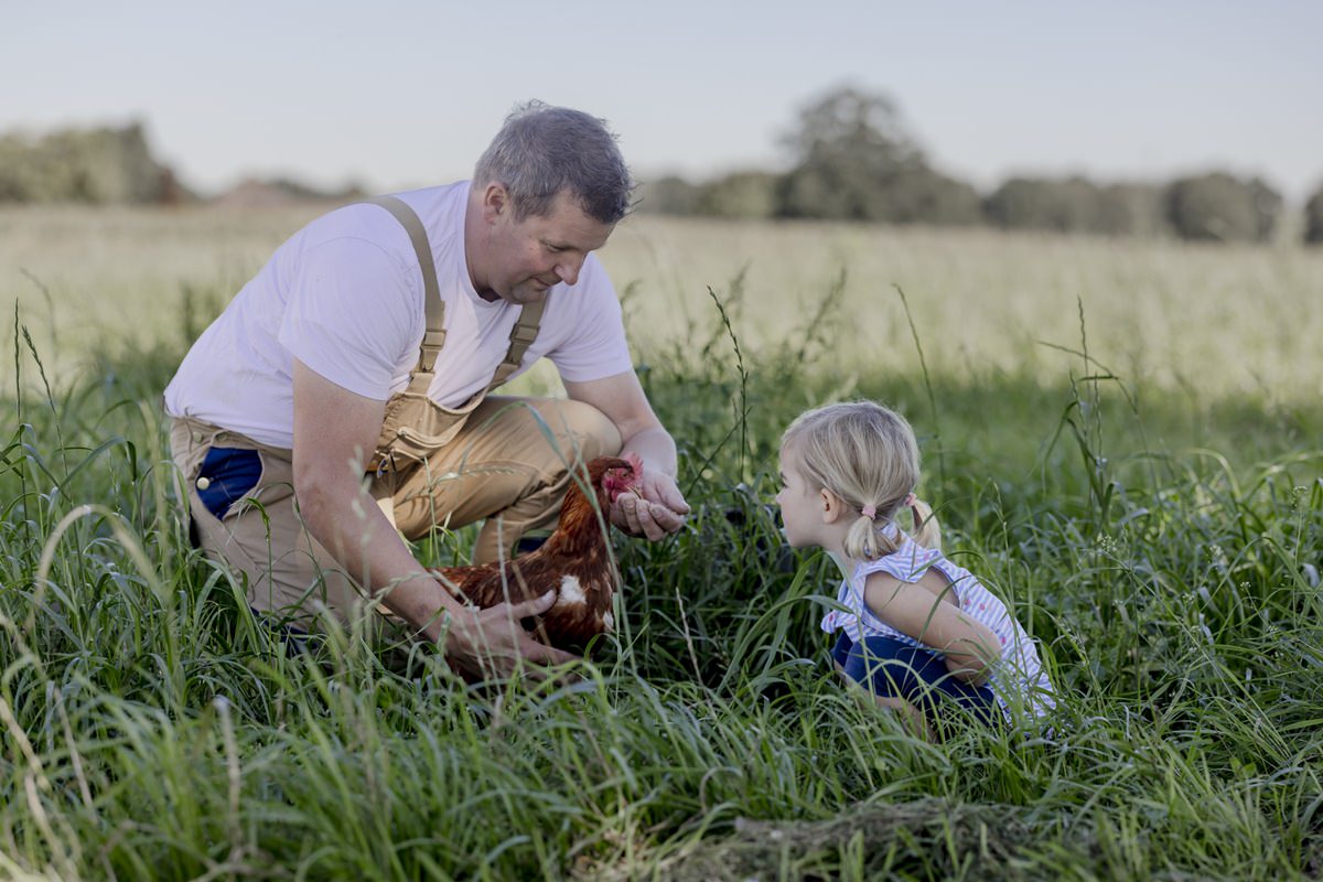 ein Landwirt füttert mit seiner Tochter ein Huhn auf der Wiese | Foto: Hanna Witte