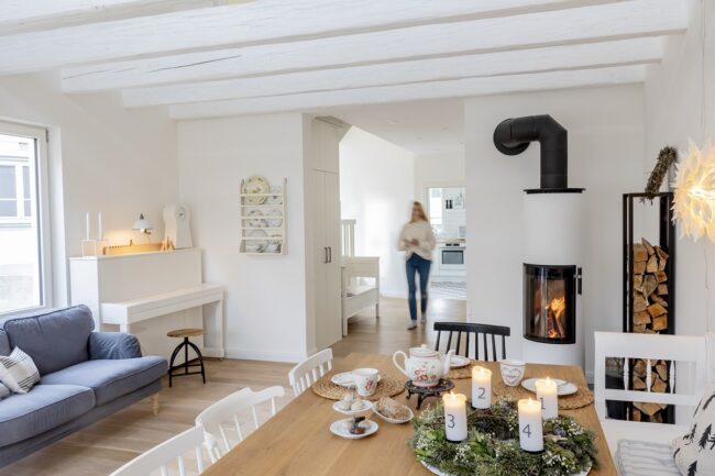 weißer Wohnbereich mit Ofen, Klavier, Esstisch und hellblauem SofaTrockenblumen und Nüsse liegen auf einer großen goldenen Platte | Foto: Hanna Witte